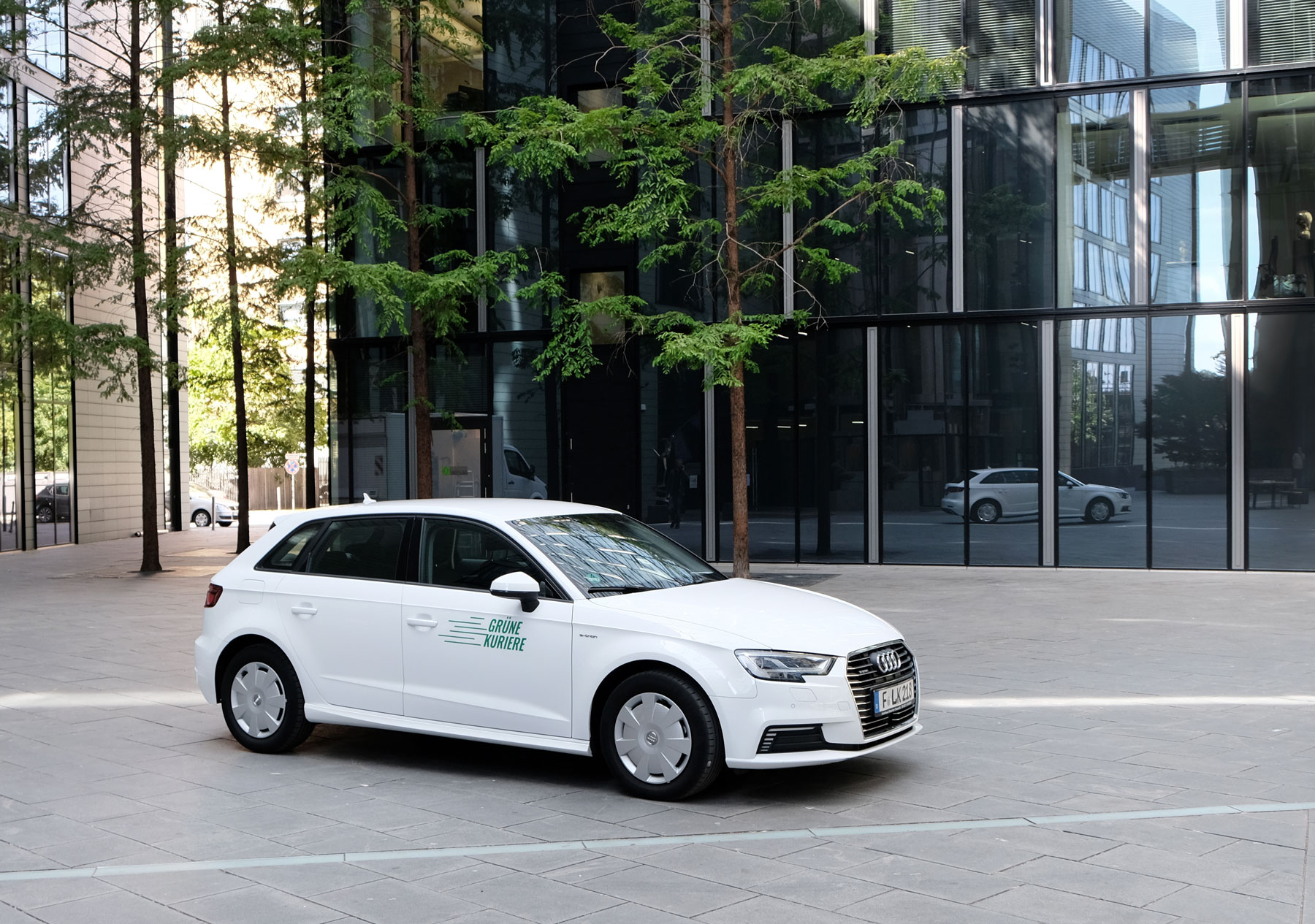 weißes Elektroauto vor Glasfassade mit Logo der Grünen Kuriere